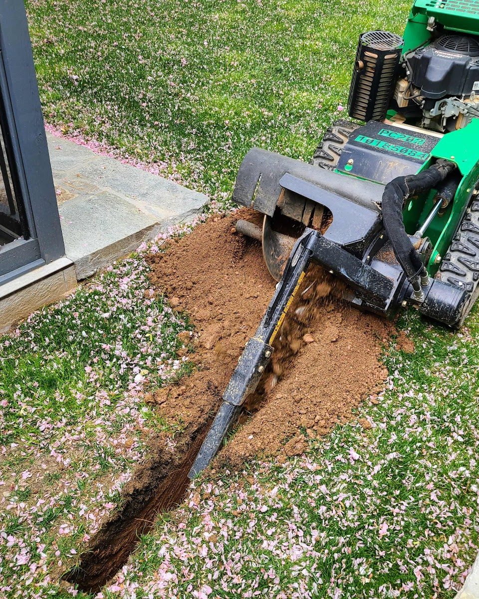 French drain trench being cut along a foundation wall for drainage installation