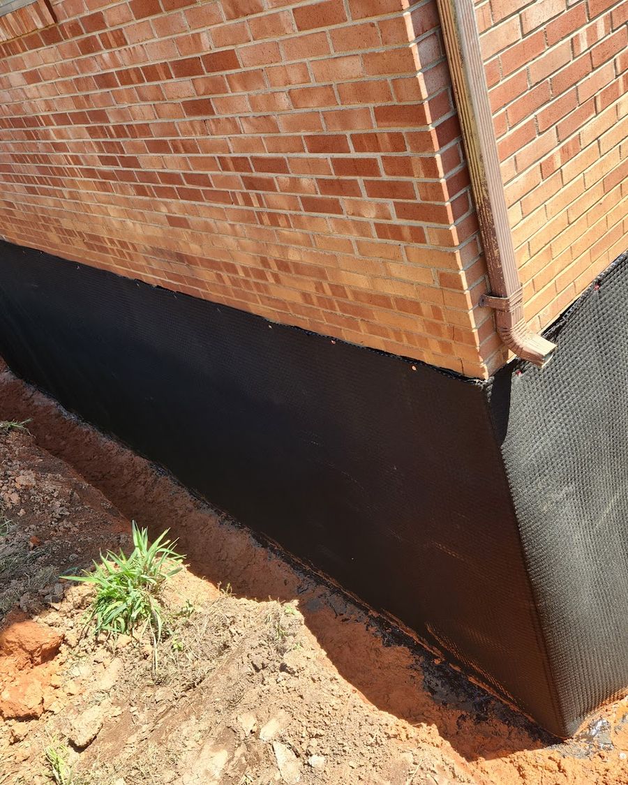 Exterior waterproofing membrane and drainage mat installed at a brick home's foundation corner