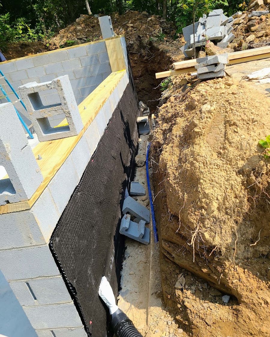 Block foundation wall with waterproofing membrane and drainage board along a new trench